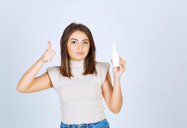 Femme souriante avec un spray montrant un pouce vers le haut.