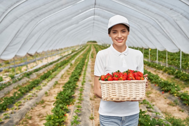 Femme souriante tenant un panier avec des fraises mûres rouges