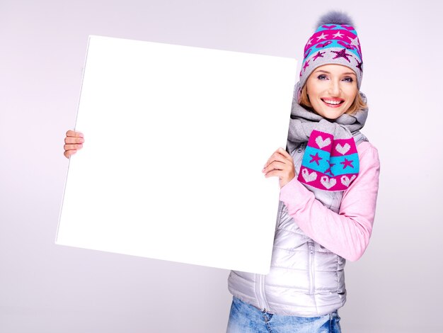 Femme souriante en vêtements d'extérieur d'hiver tient la pancarte blanche dans les mains