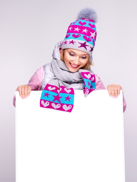 Femme souriante en vêtements d'extérieur d'hiver tient la pancarte blanche dans les mains