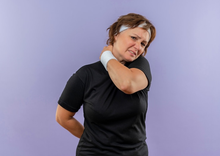 Photo gratuit femme sportive d'âge moyen en t-shirt noir avec bandeau à la recherche de mal à toucher son cou sensation de douleur debout sur le mur bleu