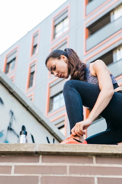 Femme sportive attachant des chaussures sur le mur de briques