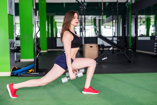 Femme sportive avec un corps solide fait différents exercices dans un club de sport moderne avec des miroirs
