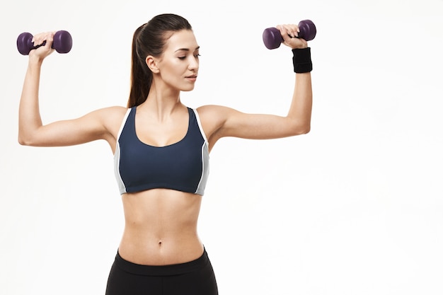 Femme sportive dans les bras de formation sportswear avec des haltères sur blanc.