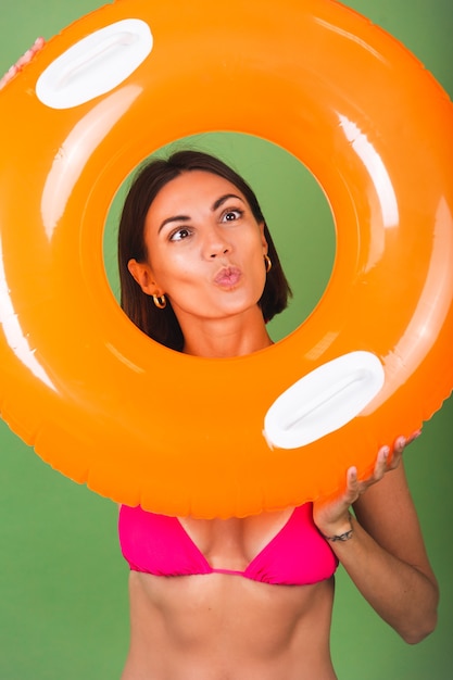 Femme sportive en forme d'été en bikini rose et anneau gonflable orange vif rond sur vert, joyeux enjoué avec des grimaces amusantes