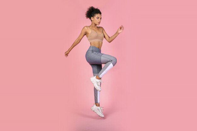 Femme sportive pratiquant des exercices de squat en studio. Femme africaine en tenue de sport travaillant sur fond rose.