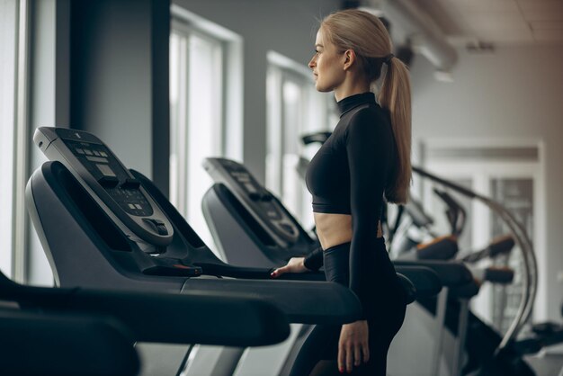 Femme sportive qui court sur tapis roulant à la salle de gym