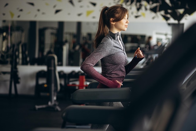 Femme sportive qui court sur tapis roulant à la salle de gym