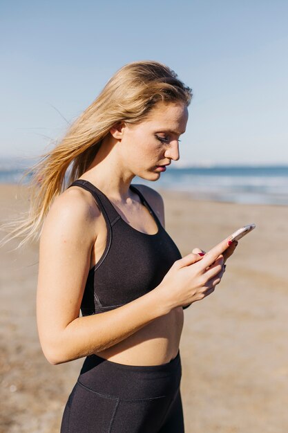 Femme sportive avec smartphone à la plage