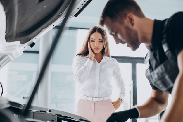 Femme à la station-service acr vérifiant sa voiture avec mécanicien