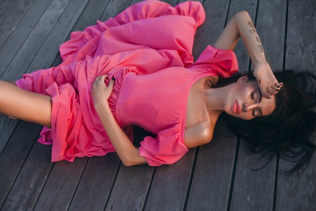 Femme de style d'été en plein air, portrait de mode ensoleillé de femme sensuelle porter une robe rose sur la plage coucher de soleil sur le bord de mer de l'océan