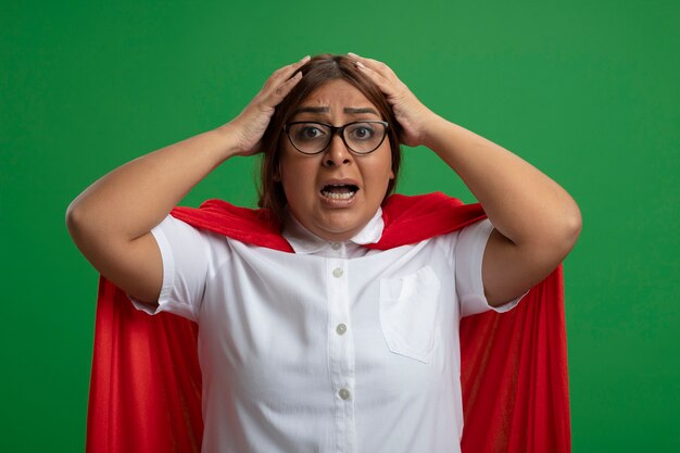 Femme de super-héros d'âge moyen effrayée portant des lunettes a saisi la tête isolée sur fond vert