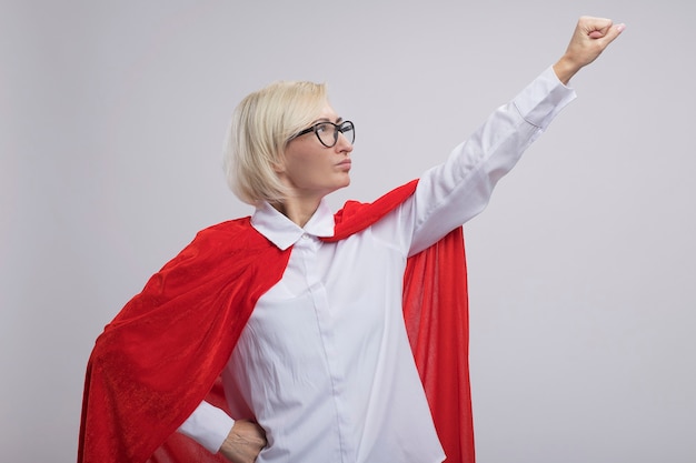 Photo gratuite femme de super-héros blonde d'âge moyen confiante en cape rouge portant des lunettes jusqu'à faire le geste de superman