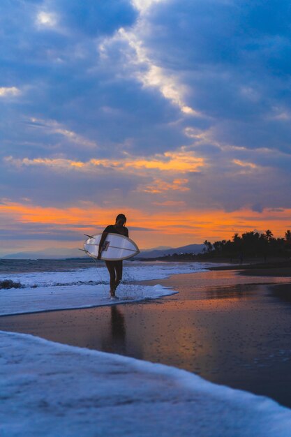 Femme surfeuse avec planche de surf sur l'océan au coucher du soleil.