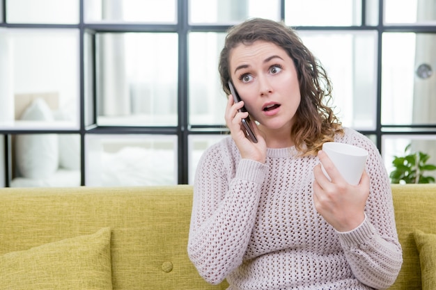 Une femme surpris qui parle au téléphone et boit du thé