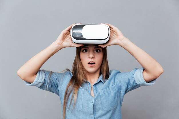 Femme surprise en chemise décolle d'un appareil de réalité virtuelle