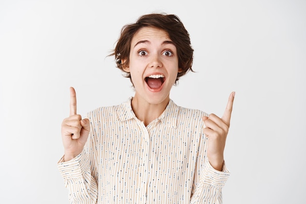 Femme surprise hurlant d'excitation et de joie pointant les doigts vers le haut montrant une publicité sur fond blanc