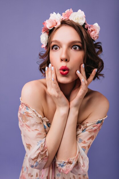 Femme surprise avec maquillage élégant et manucure posant. Phofo intérieur de fille étonnée dans un cercle de fleurs isolées.