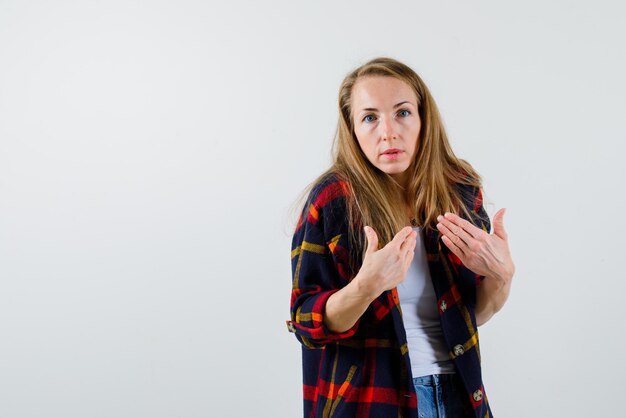 La femme surprise se montre avec les mains sur fond blanc