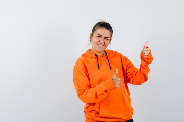 Femme en sweat à capuche orange montrant le double pouce vers le haut et l'air heureux