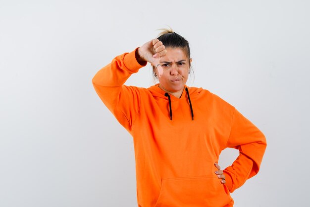 Femme en sweat à capuche orange montrant le pouce vers le bas et à la sombre