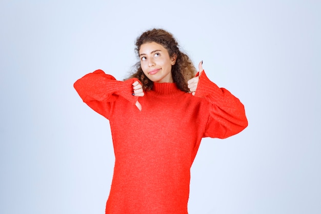 femme en sweat-shirt rouge montrant des signes de pouce vers le haut et vers le bas.