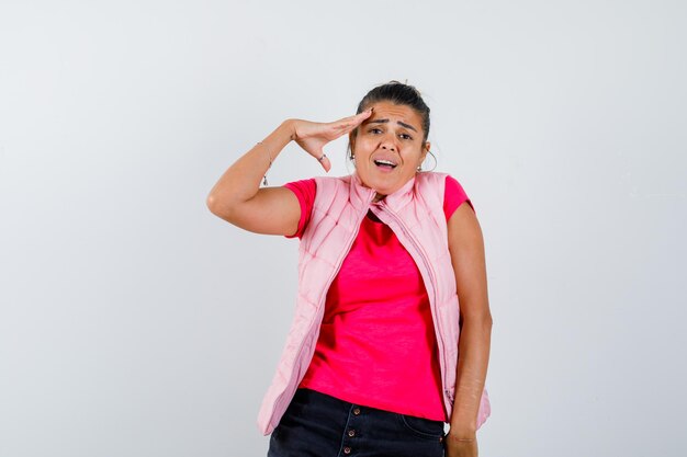 Femme en t-shirt, gilet montrant un geste de salut et ayant l'air effrayé