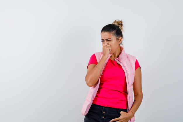 Femme en t-shirt, gilet pinçant le nez, sentant une mauvaise odeur et ayant l'air dégoûté