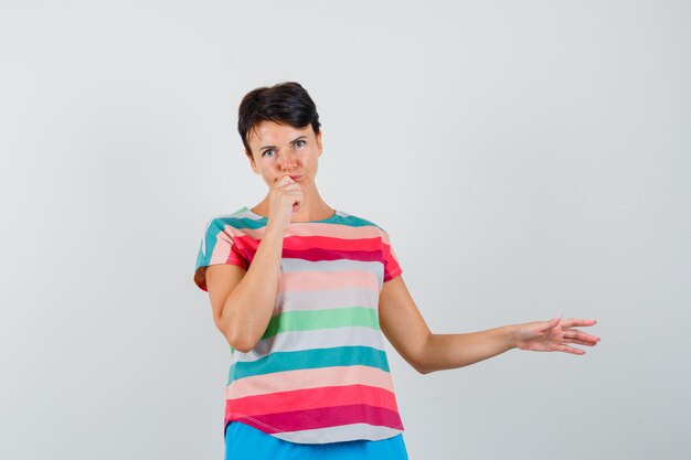 Femme en t-shirt rayé, pantalon écartant le bras tout en pensant et à l'hésitation