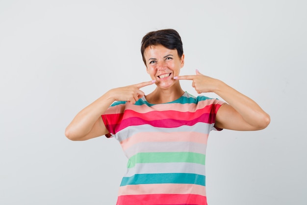 Femme en t-shirt rayé pointant sur ses dents et à la joyeuse