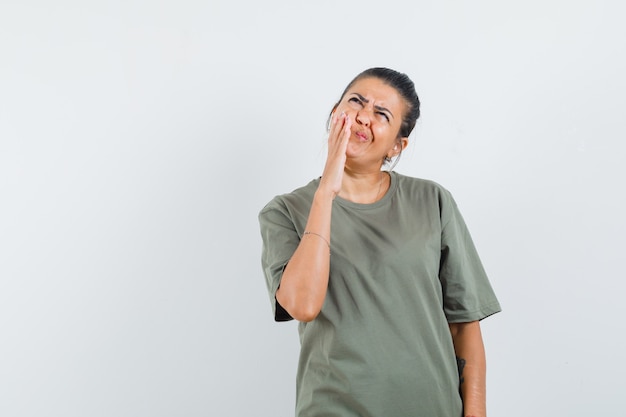 Femme en t-shirt tenant la main sur la joue et à l'hésitation