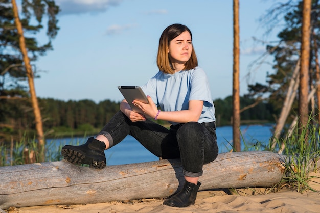 Photo gratuite femme avec tablette assis près du lac