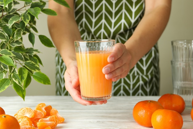 Femme en tablier tient un verre avec du jus de mandarine, gros plan