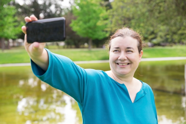 Femme de taille plus gaie prenant selfie dans le parc