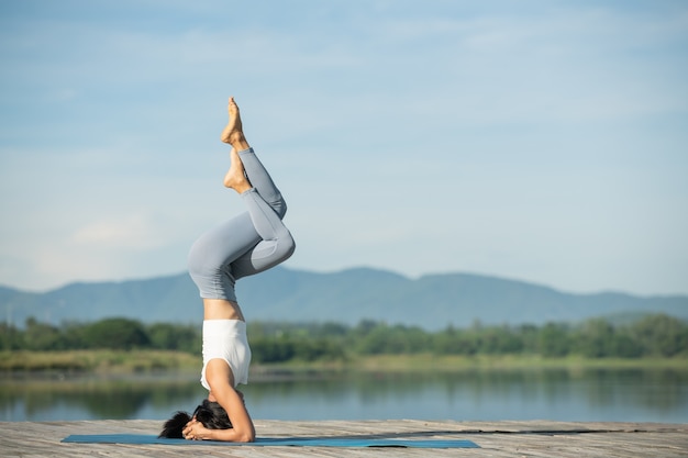 Femme sur un tapis de yoga pour se détendre dans le parc. Jeune femme asiatique sportive pratiquant le yoga, faisant des exercices de poirier, s'entraînant, portant des vêtements de sport, des pantalons et un haut.