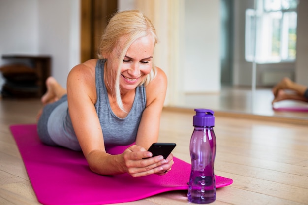 Photo gratuite femme sur un tapis de yoga vérifiant son téléphone