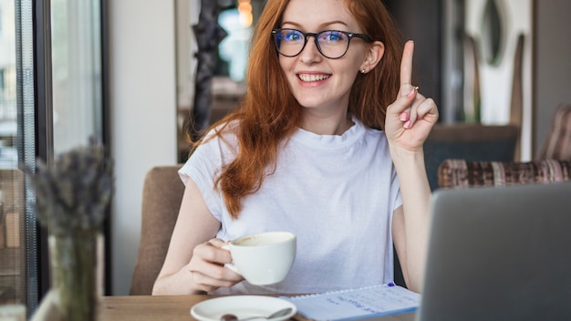 Femme avec une tasse de café montrant un doigt pointé