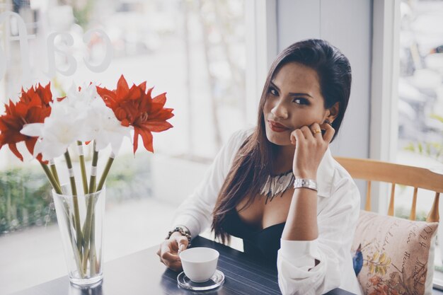 Femme avec une tasse de café et un vase avec des fleurs rouges