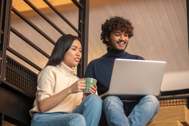 Femme avec tasse et homme regardant un ordinateur portable