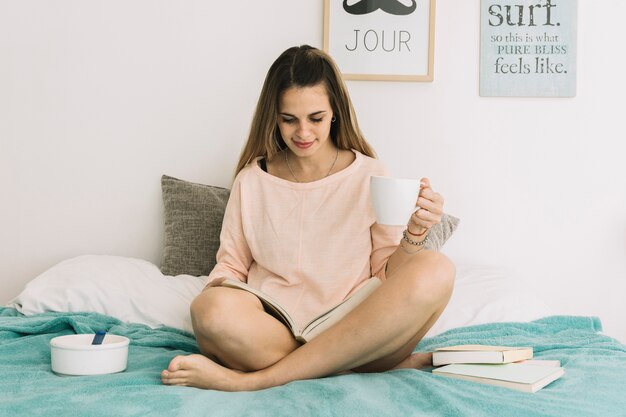 Femme, à, tasse, lecture, livre, lit