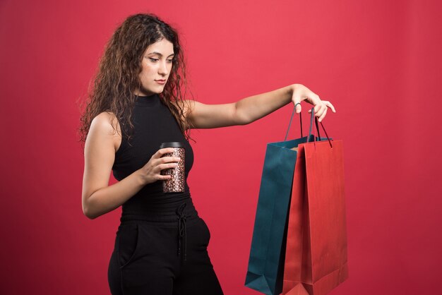 Femme avec tasse montrant ses deux sacs de nouveaux vêtements sur fond rouge