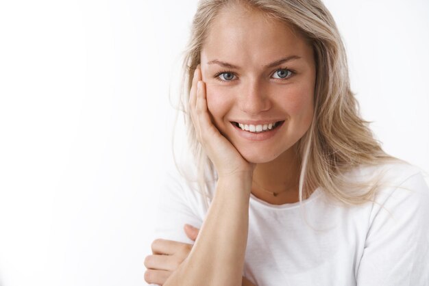 femme avec un tatouage s'appuyant sur le bras et regardant avec un regard sensuel affectueux à la caméra souriant belle à la caméra exprimant de la tendresse des sentiments doux sur un mur blanc