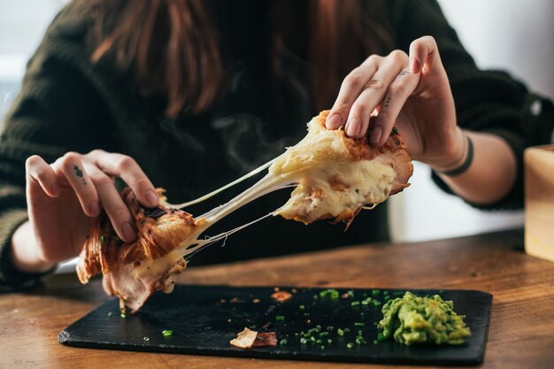 Femme avec des tatouages sur les doigts se brise prêt à manger un croissant avec du fromage fondu et du jambon