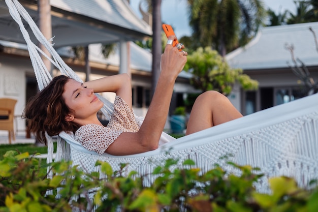 Femme avec téléphone reposant allongé sur un hamac avec téléphone mobile