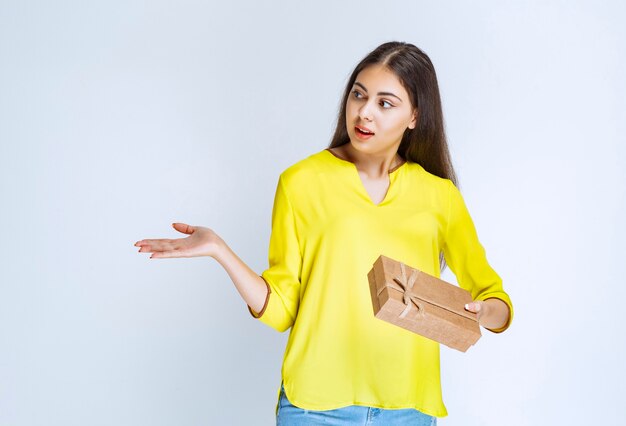 femme tenant une boîte-cadeau en carton et pointant du doigt quelqu'un de côté.