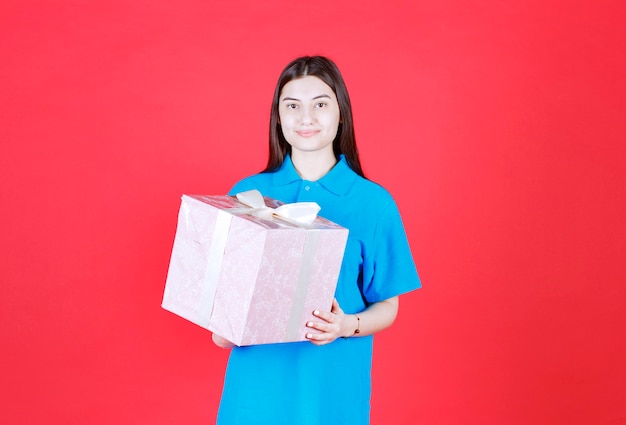 femme tenant une boîte cadeau violette enveloppée de ruban blanc.