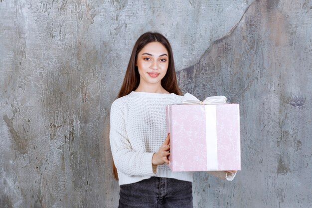 femme tenant une boîte cadeau violette enveloppée de ruban blanc.