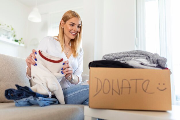 Femme tenant une boîte de don avec plein de vêtements Femme tenant un livre et une boîte de don de vêtements Vêtements dans une boîte pour le don de concept et le recyclage