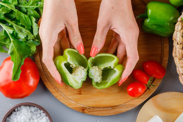 Femme tenant du poivre vert coupé en deux sur une planche à découper avec des tomates, du sel et du fromage