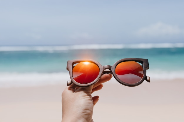 Femme tenant des lunettes de soleil d'été élégantes sur la mer. Photo extérieure de la main féminine avec des lunettes à la plage.